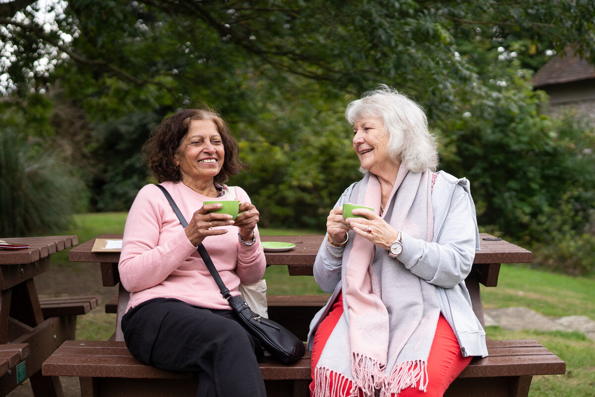 Two people, sitting on a picnic bench, smiling and holding cups