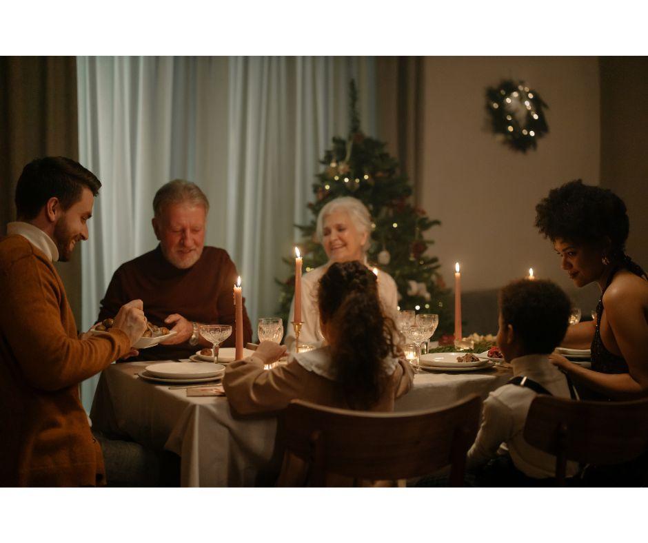 Group of people sitting round a candlelit dining table sharing food.