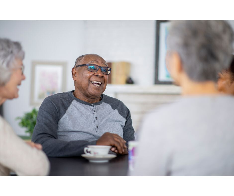 Group of people sitting together at a table, laughing and having a cup of tea